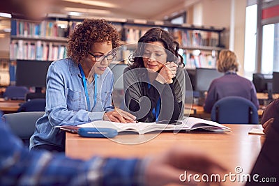 Teacher With Mature Female Adult Student Sitting At Table Working In College Library Stock Photo