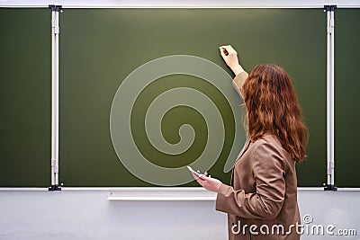 Teacher with a phone in hand writes a text in chalk on a school blackboard, copy space Stock Photo