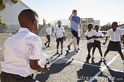 Teacher plays football with young kids in school playground Stock Photo