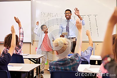 Teacher and pupil with raised hands at front of school class Stock Photo