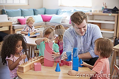 Teacher And Pupils Working At Tables In Montessori School Stock Photo