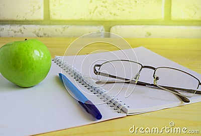 Teacher's Day concept and back to school, green Apple, book, laptop, reading glasses and pen on wooden table, sunlight Stock Photo