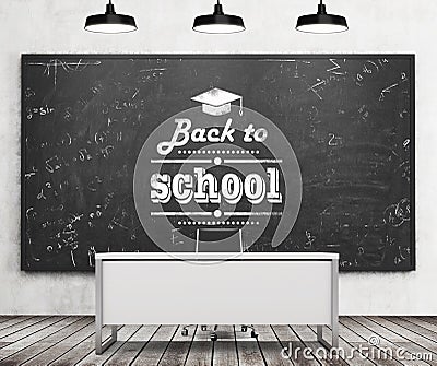 Teacher's desk in a modern university or school. A huge black chalkboard on the wall with written down phrase - Back to school. Stock Photo