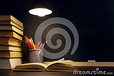 The teacher`s desk or a worker, on which the writing materials lie, a books, in the evening under the lamp. Blank for text or Stock Photo