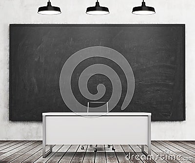 Teacher's or professor's desk in a modern university. A huge black chalkboard on the wall and three black ceiling lights, wooden f Stock Photo