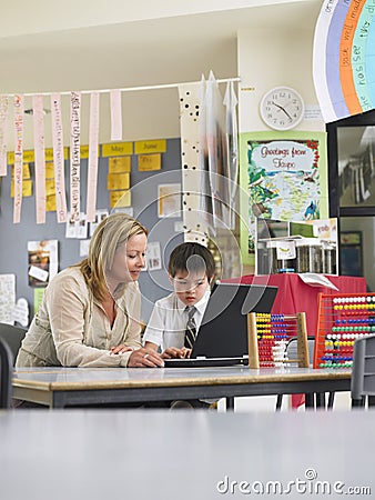 Teacher Sitting With Boy Using Laptop In Class Stock Photo