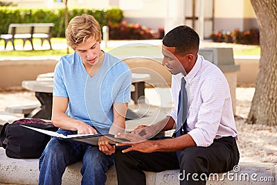 Teacher Sitting Outdoors Helping Male Student With Work Stock Photo