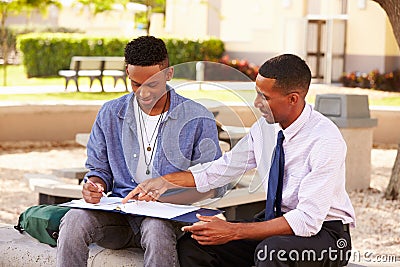 Teacher Sitting Outdoors Helping Male Student With Work Stock Photo