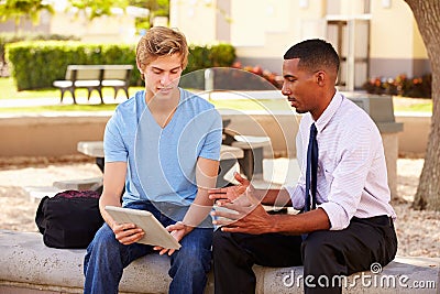 Teacher Sitting Outdoors Helping Male Student With Work Stock Photo