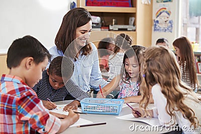 Teacher sitting at table with young school kids in lesson Stock Photo
