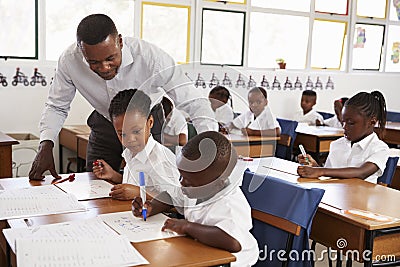 Teacher stands helping elementary school kids at their desks Stock Photo