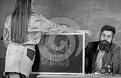 Teacher strict sit table chalkboard background. Student in mini skirt with nice buttocks stand near blackboard. School Stock Photo