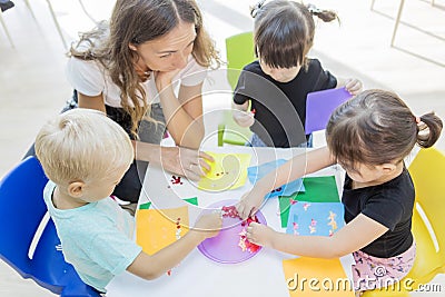 Teacher and students gluing trinkets on a paper Stock Photo