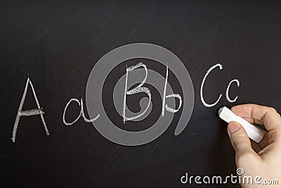 Teacher is writing letter of alphabet on blackboard with chalk. Stock Photo