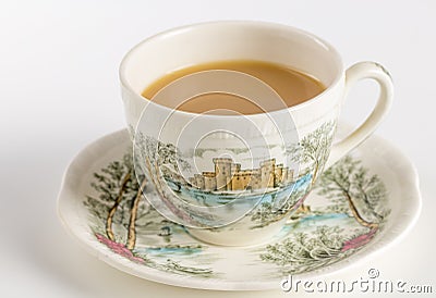 Teacup with tea and saucer decorated with English castle scene - Stock Photo