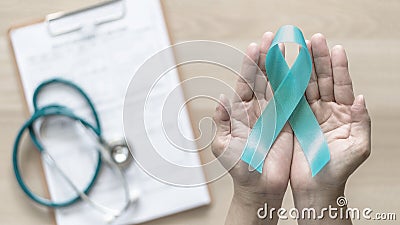Teal ribbon awareness on woman`s hand for Ovarian Cancer, Polycystic Ovary Syndrome PCOS disease, Post Traumatic Stress Disorder Stock Photo
