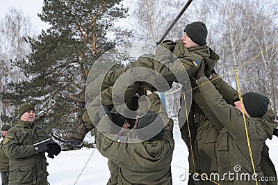 Team-building exercise: soldiers holding their fellow on hands pushing him through net Editorial Stock Photo