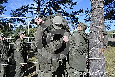 Team-building exercise: soldiers holding their fellow on hands pushing him through rope net. Novo-Petrivtsi military base, Ukraine Editorial Stock Photo