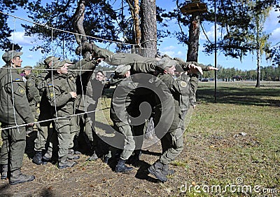 Team-building exercise: soldiers holding their fellow on hands pushing him through rope net. Novo-Petrivtsi military base, Ukraine Editorial Stock Photo