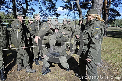 Team-building exercise: soldiers holding their fellow on hands pushing him through rope net. Novo-Petrivtsi military base, Ukraine Editorial Stock Photo