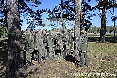 Team-building exercise: soldiers holding their fellow on hands pushing him through rope net. Novo-Petrivtsi military base, Ukraine Editorial Stock Photo