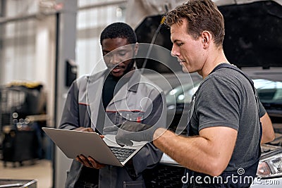Team Of Diverse Auto Mechanic And Repairman Checking Diagnostics Results on Laptop. Stock Photo