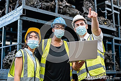 Team engineering three nationality wear face mask uniform working with computer laptop at factory. Stock Photo