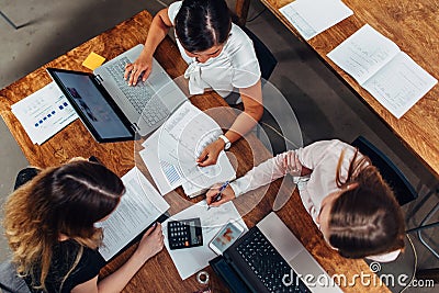 Team of female accountants preparing annual financial report working with papers using laptops sitting at desk in office Stock Photo