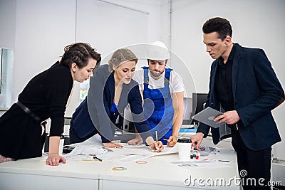 Team of four young architects working on a new project and communicating while analyzing blueprints in the office Stock Photo