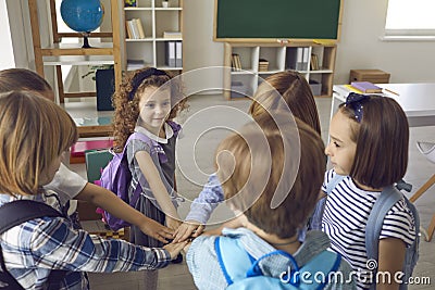 Team of happy little school children standing in the classroom and holding hands together Stock Photo