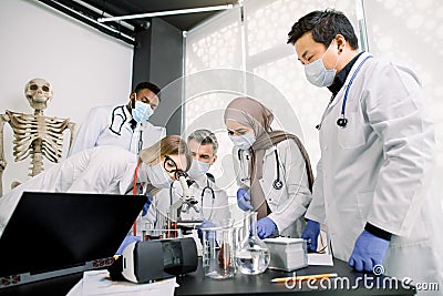 Team of lab workers, veterinarians, bio chemists examining tissues or blood sample using the microscope. Group of Stock Photo