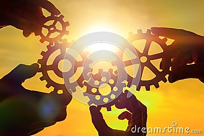 Team of people with gears in hands on sunset background. Stock Photo