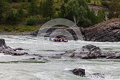 A team of people rafting in orange life jackets on an rubber boat of blue and yellow colors along a mountain river against the Editorial Stock Photo