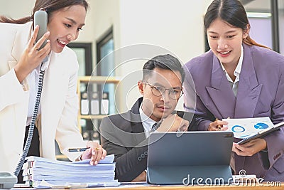 A team of three Asian businessmen is working inside an office where businessmen in black suits are being ordered by their Stock Photo