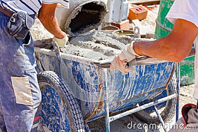 Team of workers are pouring concrete from cement mixer into wheelbarrow Stock Photo