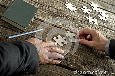 Teamwork and cooperation between two business people as they join forces to combine matching puzzle pieces Stock Photo