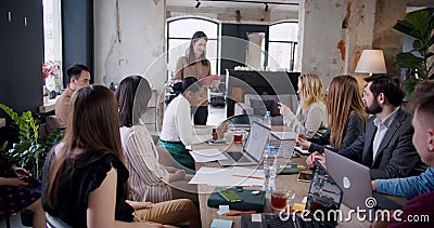 Teamwork at modern trendy coworking. Successful young brunette female business coach leading multiethnic office seminar. Stock Photo