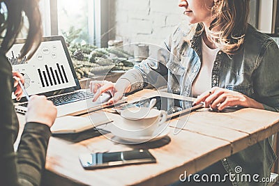 Teamwork. Two young business woman sitting at table in coffee shop, look at chart on laptop screen and develop business plan. Stock Photo
