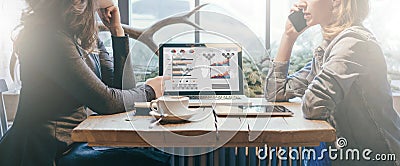 Teamwork, two young businesswomen sitting across table from each other. On table laptop, coffee cup and tablet computer. Stock Photo