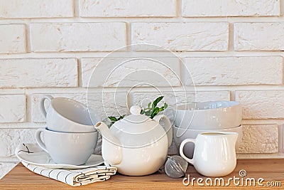 Teapot, cups and other tableware on the wooden table near the brick wall. Stock Photo