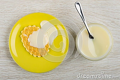 Teaspoon in bowl with condensed milk, cookie with milk in saucer on wooden table. Top view Stock Photo