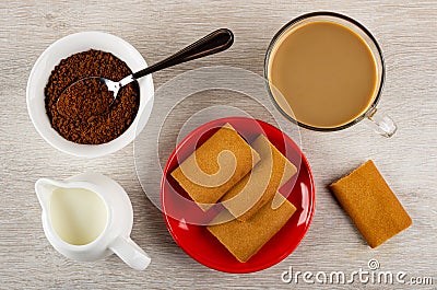 Spoon in bowl with instant coffee, cup of coffee with milk, jug of milk, cookies with filling in red saucer on table. Top view Stock Photo