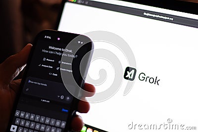 Tech guy trying out Grok in mobile phone with the laptop screen showing Grok logo, an generative, conversational, neural network, Editorial Stock Photo