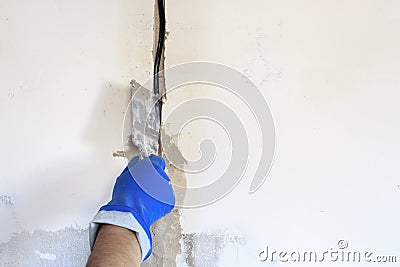 . technical hole in it is an electrical wire. the wall is white. Master with a spatula and mortar covers the cable Stock Photo