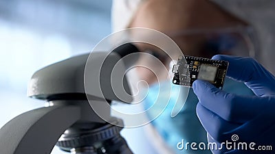 Technician examining chip, using microscope to run diagnosis and upgrade device Stock Photo