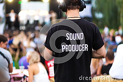 Technician guy in headphones and t-shirt with the inscription sound producer on his back at a outdoor show Editorial Stock Photo