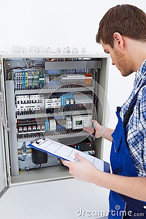 Technician holding clipboard while examining fusebox Stock Photo