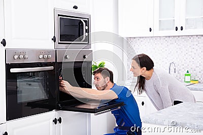 Technician In Overall Fixing Oven In Kitchen Stock Photo