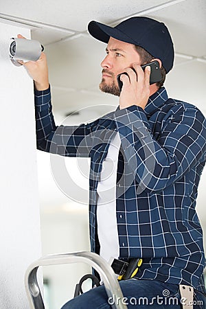 technician on phone fixing cctv camera on wall Stock Photo