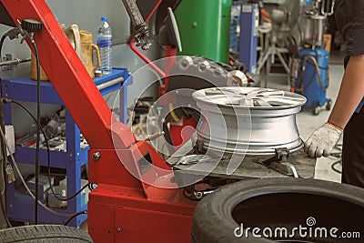 Technician removing rubber from car wheel disc & balancing tyre on balancer in auto repair garage Stock Photo